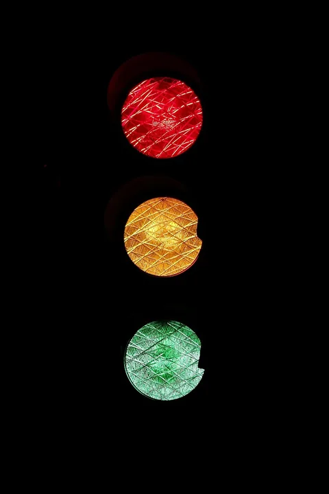 Traffic light showing red, amber and green lamps against a black background