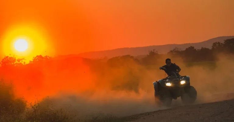 ATV rider crossing a dusty trail at sunset