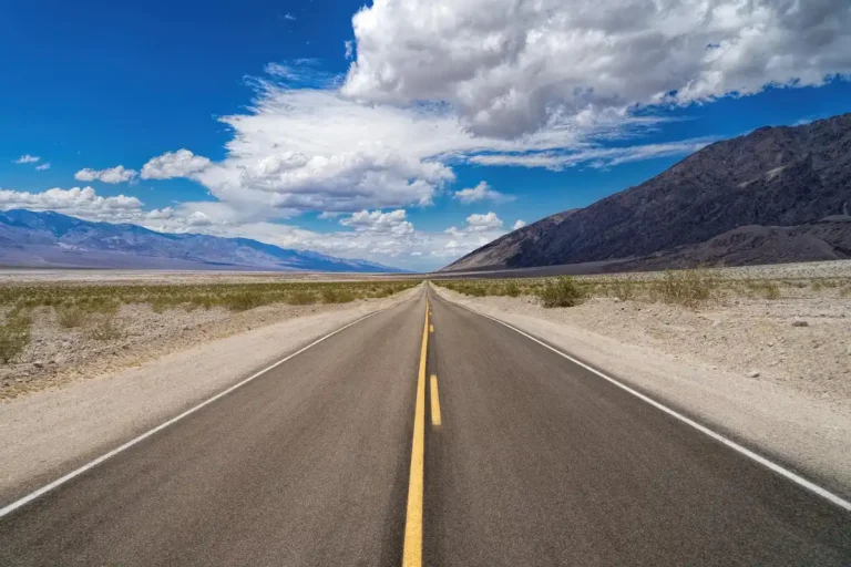 Open two-lane road under a clear blue sky with mountains in the distance