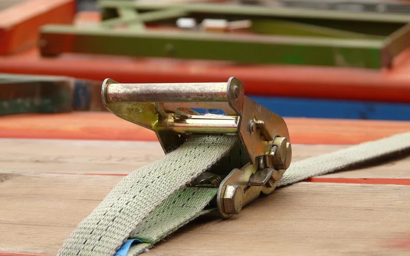 Close-up of a ratchet tie-down strap tightened over a stack of cargo