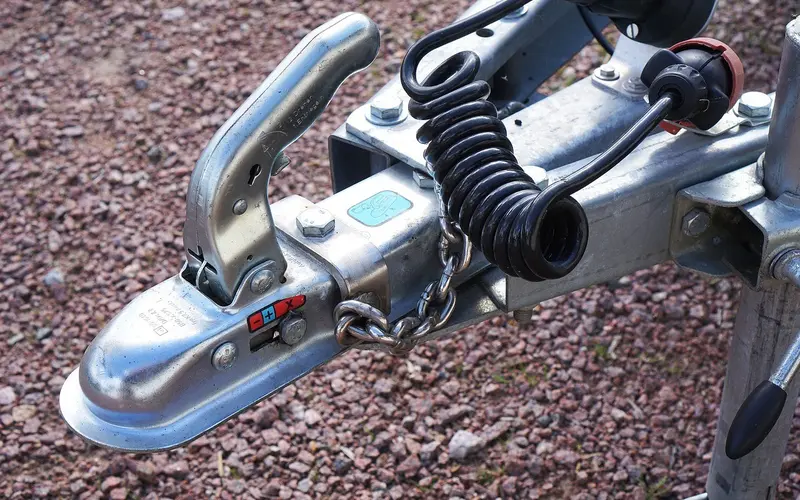 Close-up of a trailer coupling with a safety chain and a coiled electrical cable
