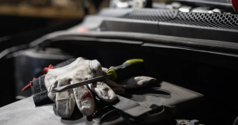Mechanic gloves and a tool resting on an open car engine bay