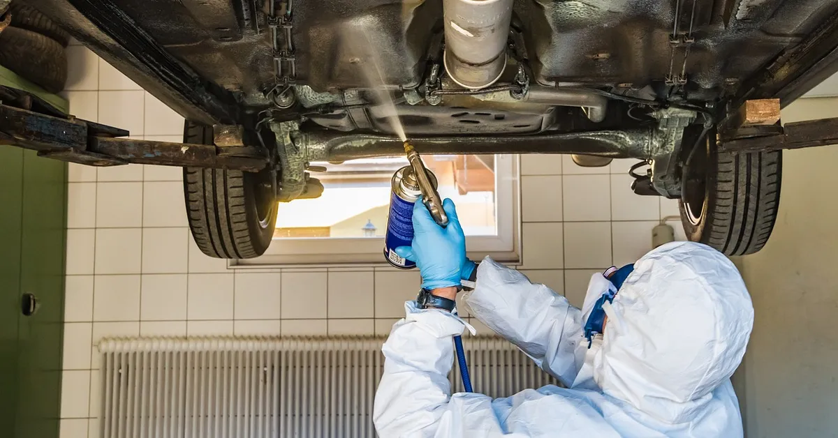 Technician spraying rust protection on a car's underbody frame