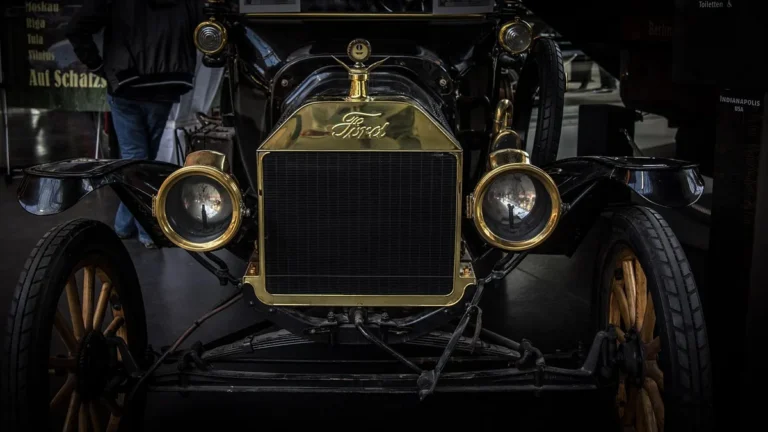 Front of a vintage Ford car with a brass radiator and headlamps on display