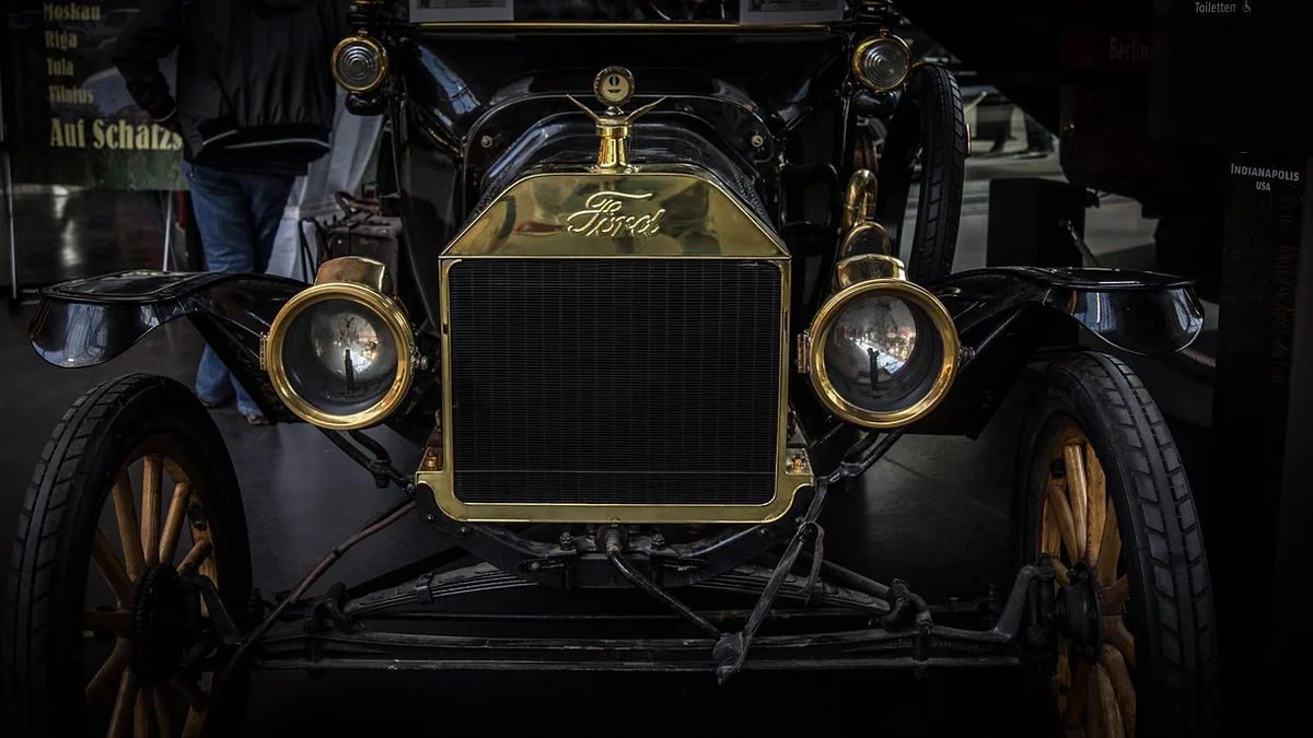 Front of a vintage Ford car with a brass radiator and headlamps on display