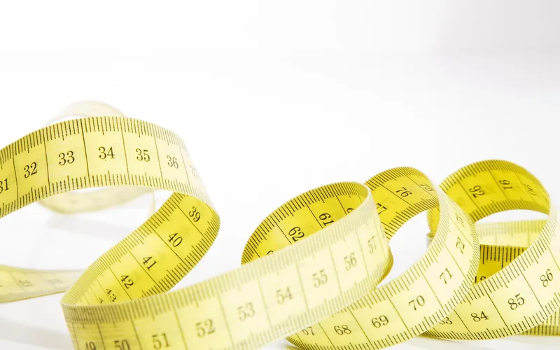 Yellow flexible measuring tape coiled on a white surface