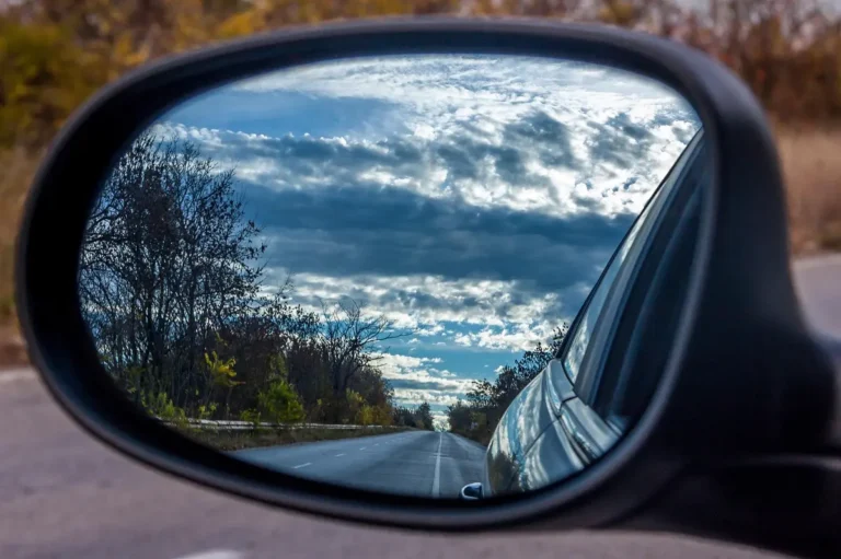 Side mirror of a car reflecting an empty road and cloudy sky