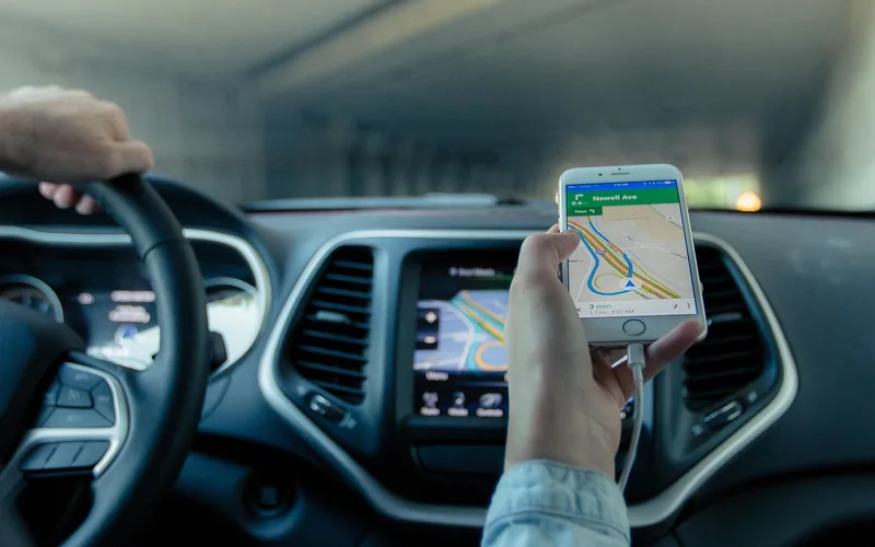 Hand holding a smartphone that shows a navigation map inside a car