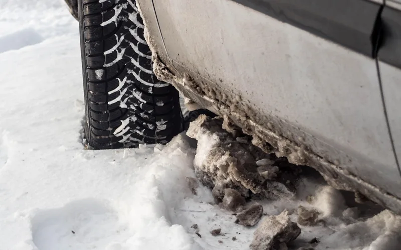Car tire with winter tread standing in snow and slush beside the car body