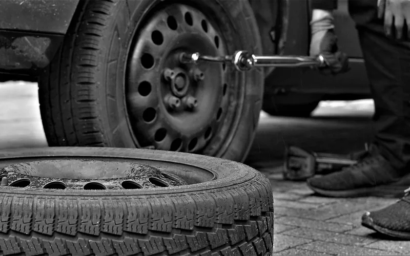 Wheel being removed from a car with a wrench, with another tire lying on the ground