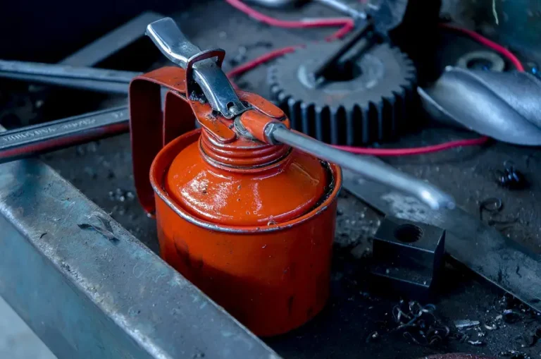 Red oil can on a workshop bench next to a gear and wrenches
