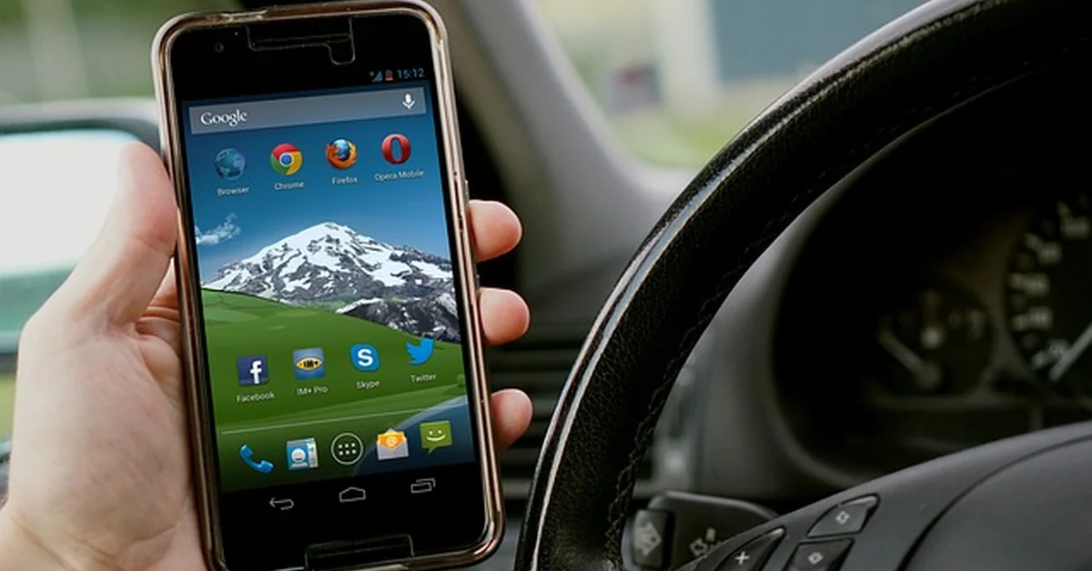 Driver using a smartphone hands-free while behind the wheel, illustrating Bluetooth phone pairing in a car