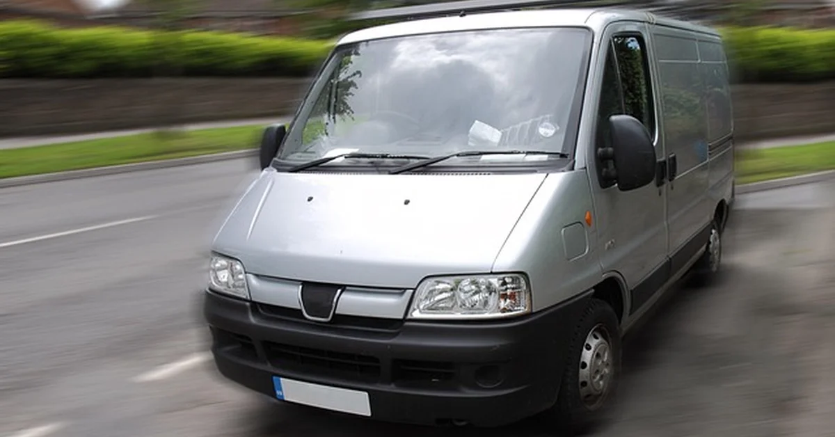 A tall cargo van driving on the road, illustrating the extra height of a Ford Transit High Roof