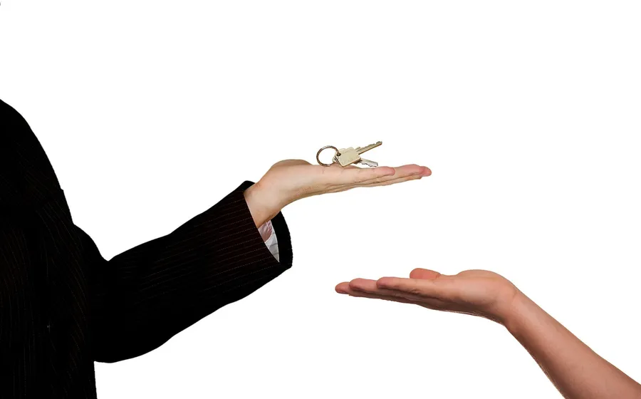 One hand holding a set of keys above an open hand, as in a key handover