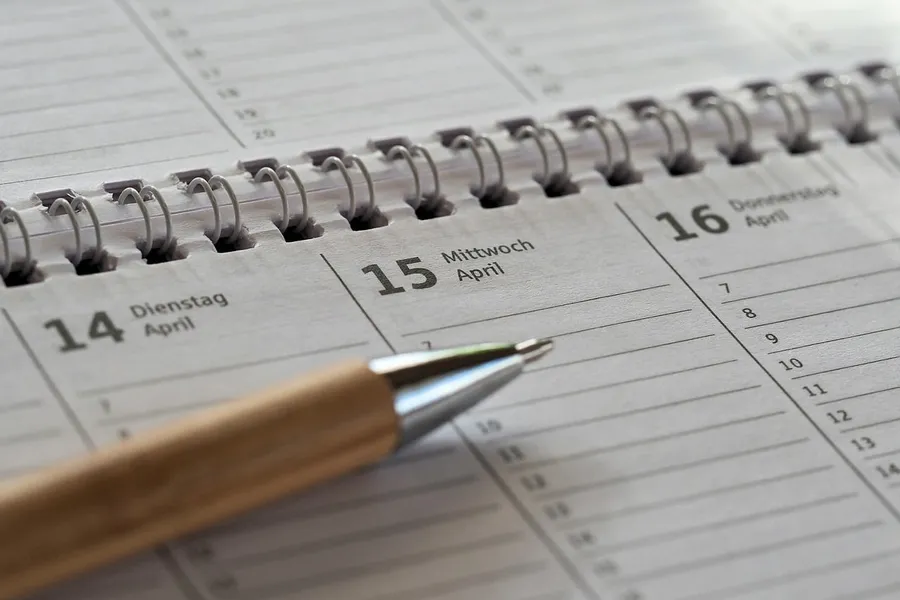 Spiral-bound desk calendar open to a week in April with a wooden pen resting on it