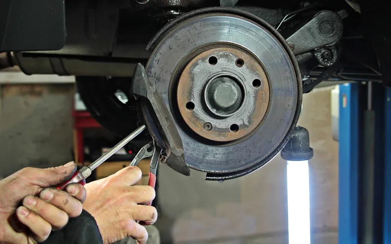Brake service on a lift during work-based automotive training Technician servicing a brake disc on a vehicle raised on a shop lifting platform