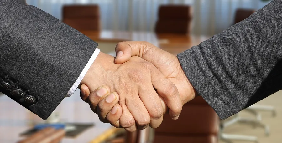 Two people in business clothes shaking hands over a conference table