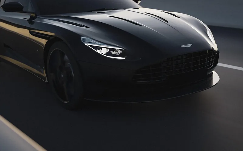 Dark grand tourer with a winged badge on the bonnet driving on a road