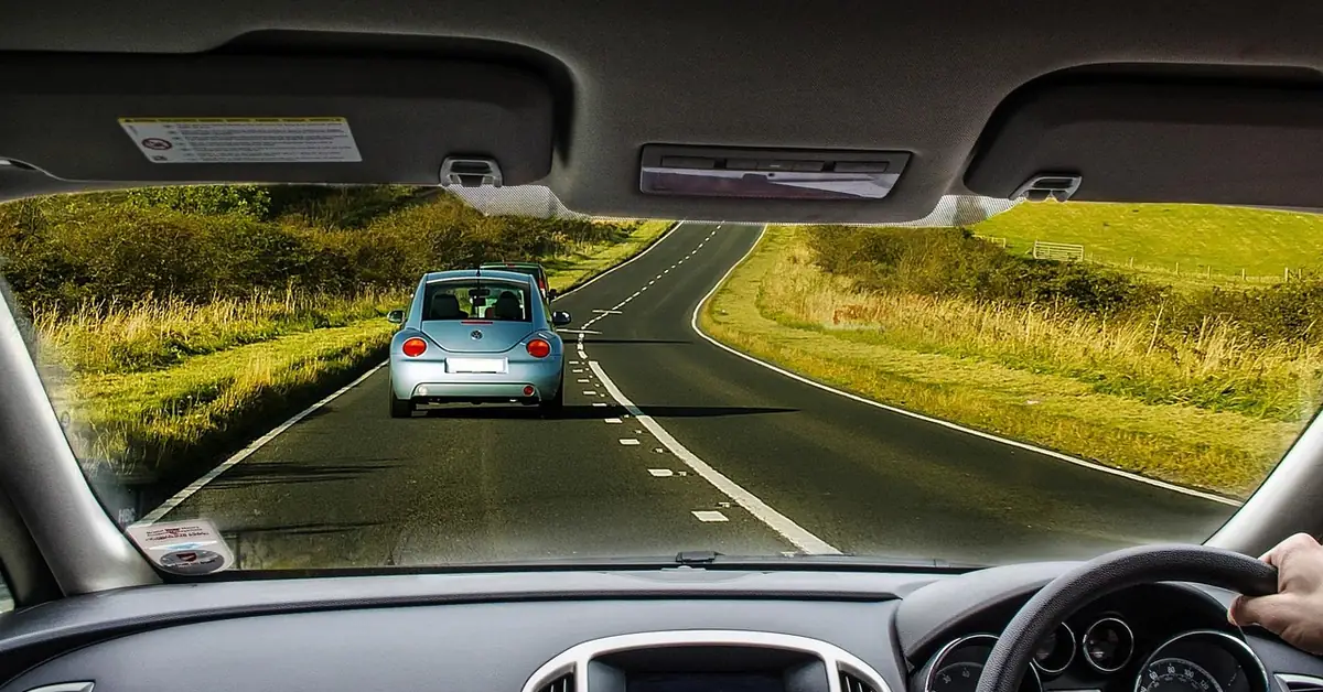 View through a car windshield of a two-lane country road with another car ahead