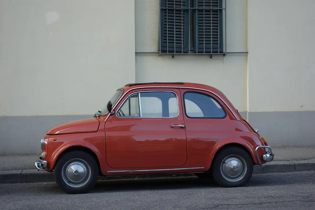 Red vintage Fiat 500 parked at the curb beside a building