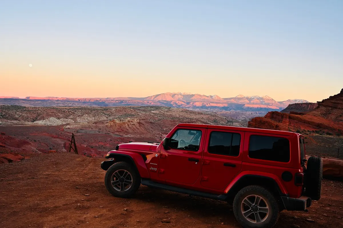 Red Jeep Wrangler parked at a desert overlook at sunset