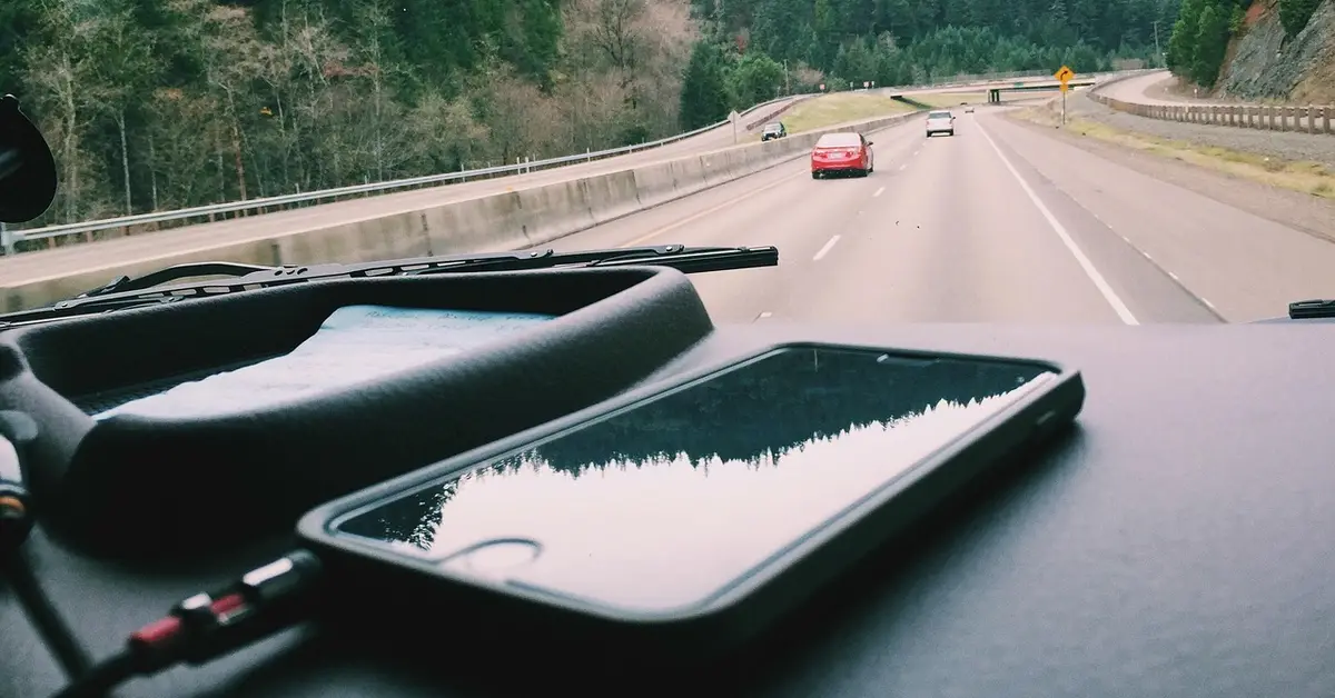 Smartphone on a car dashboard connected by an audio cable while parked on a highway view