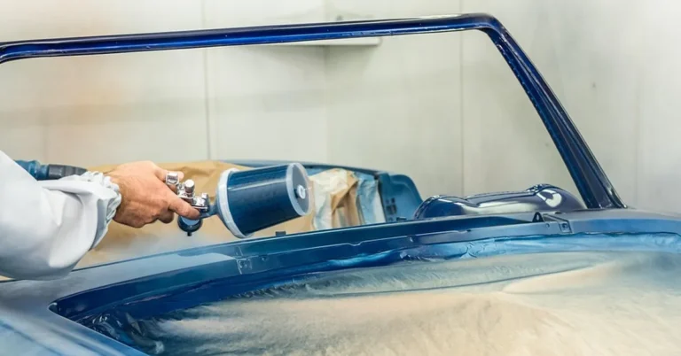 Technician spraying blue paint on a car body in a paint booth