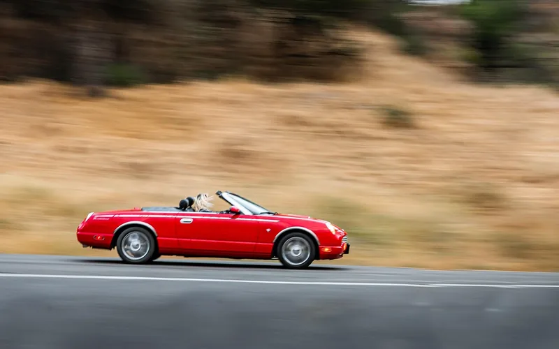 Red two-door convertible driving along a road with the roof down