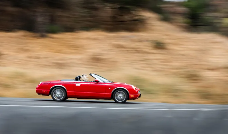Red convertible driving along an open road in a motion-blurred panning shot