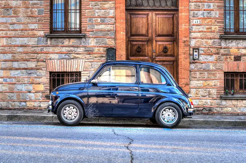 Small dark blue vintage-style city car parked beside a brick wall