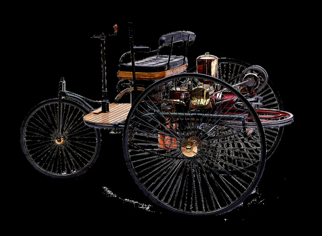 Three-wheeled early automobile with large wire-spoked wheels, a bench seat and a rear engine, shown against a black background