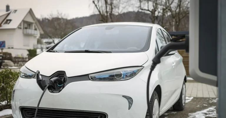 White electric hatchback plugged into a roadside charging post in winter