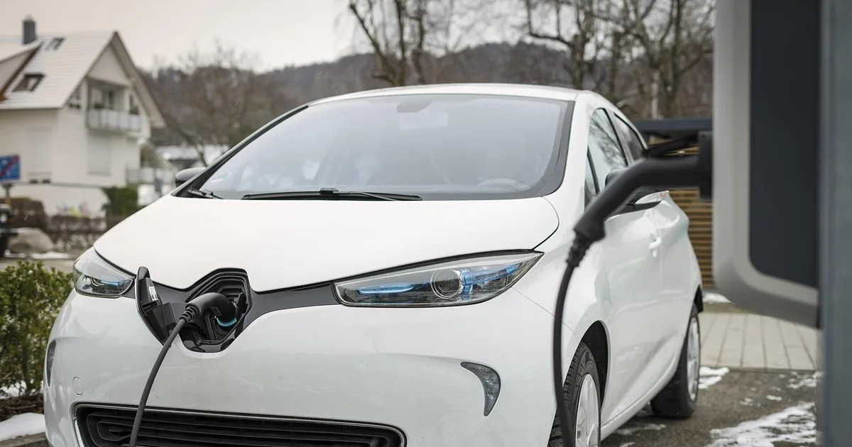 White electric hatchback plugged into a roadside charging post in winter
