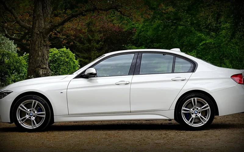 White four-door sedan seen from the side among trees