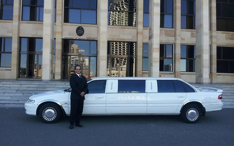 Chauffeur in a suit standing beside a luxury limousine at a curbside pickup Chauffeur in a suit standing beside a luxury limousine at a curbside pickup