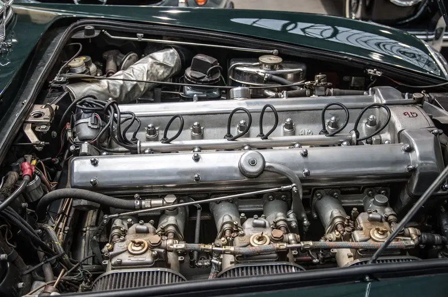 Engine bay of a classic car with a polished cam cover, carburetors and fluid reservoirs
