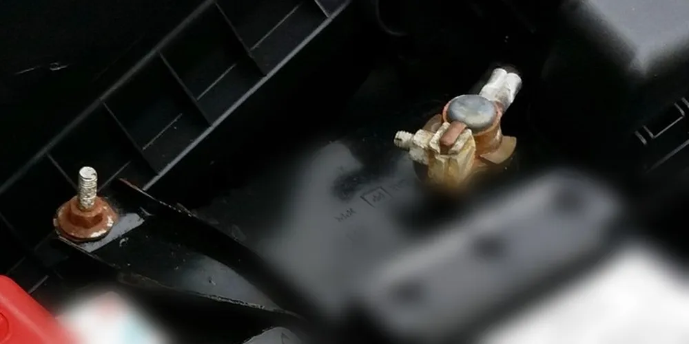 Corroded car battery terminal clamp and rusty hold-down stud in an engine bay