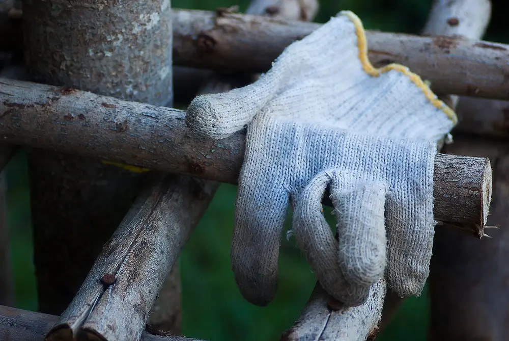 A gray knit cloth work glove with a yellow edge resting on wooden poles