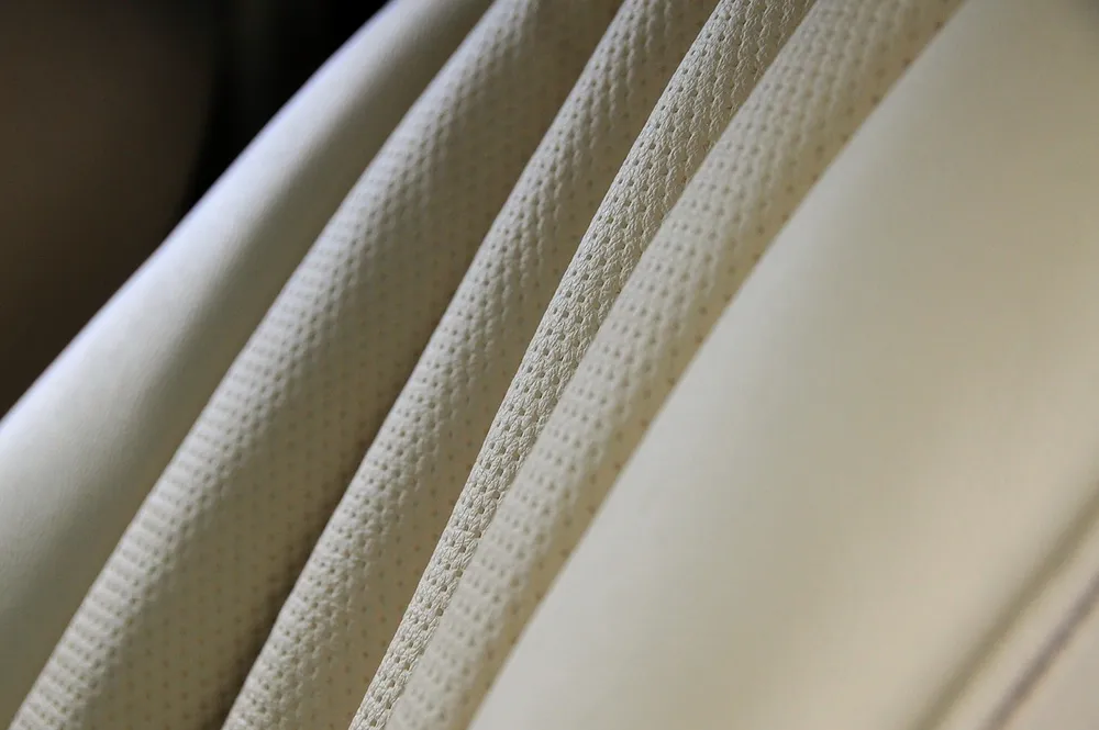Close-up of perforated cream leather seat upholstery with stitched seams