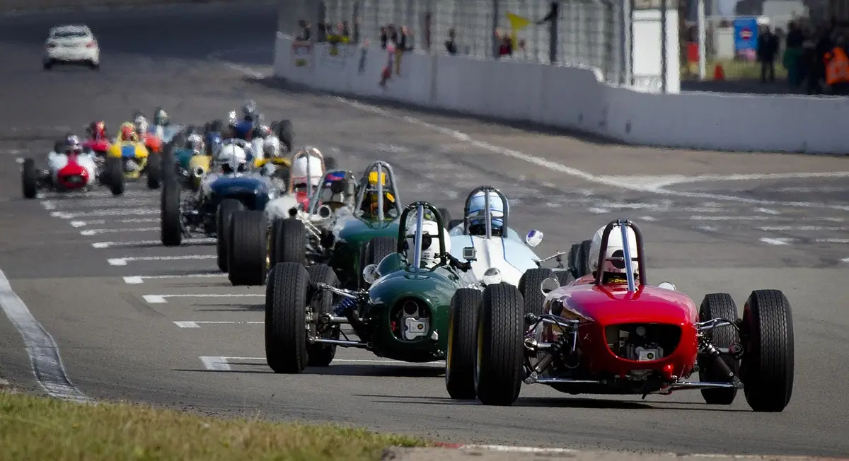 Historic open-wheel race cars lined up on a circuit straight