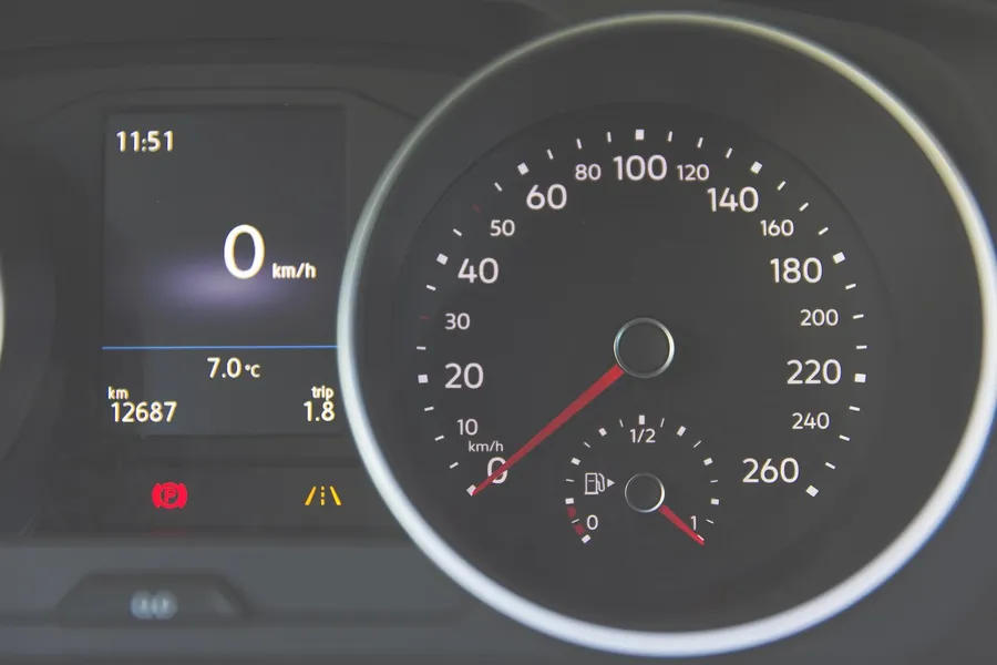 Car instrument cluster with the speedometer reading 0 km/h and a parking brake warning light