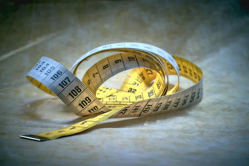 Yellow and gray measuring tape curled on a stone surface