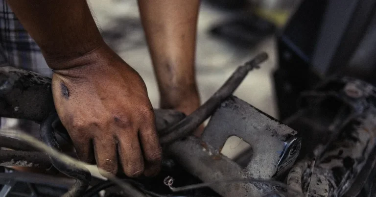 A grease-stained hand holding a cable and a metal bracket on a vehicle in a workshop