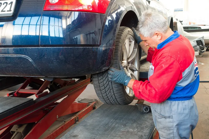 Mechanic in work clothes inspecting a car wheel on a shop lift