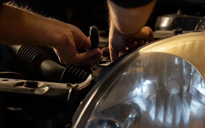 mechanic's hands working under a car hood near the engine bay during a service