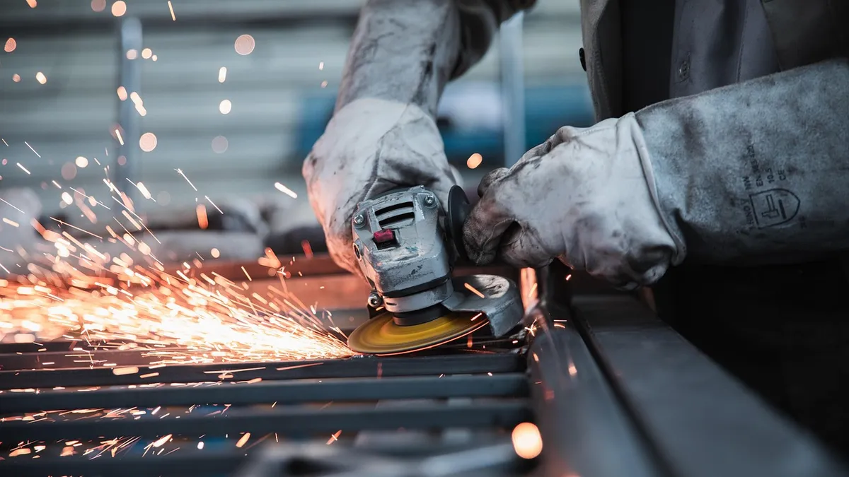 Worker in heavy gloves using an angle grinder on steel, with sparks flying
