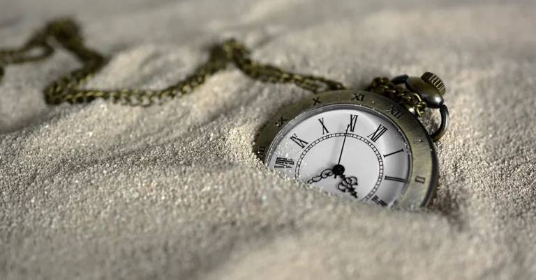 Antique pocket watch half buried in sand with a chain