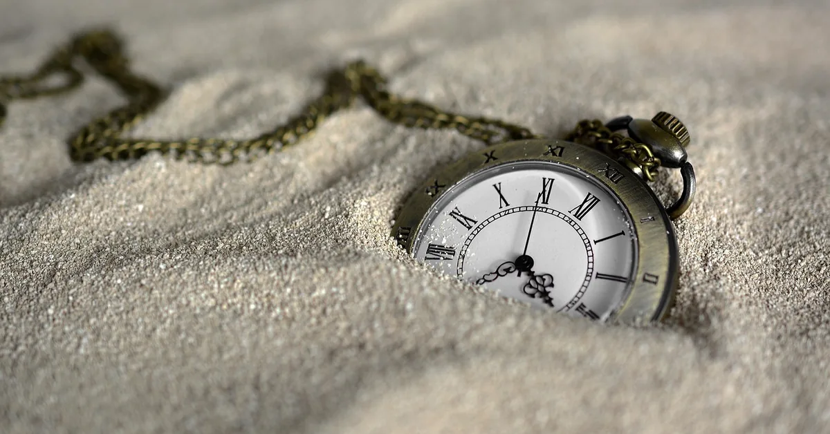 Antique pocket watch half buried in sand with a chain