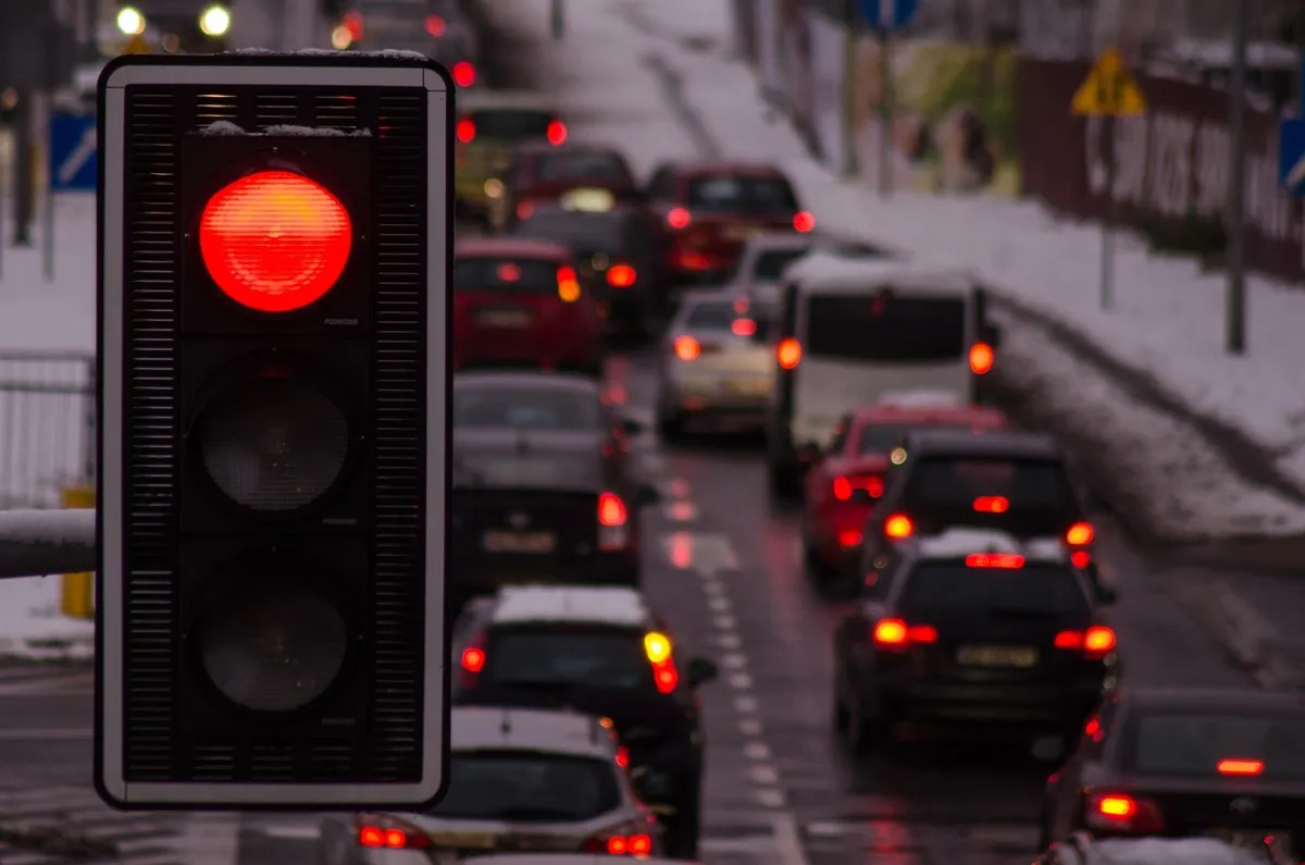 Red traffic light above a queue of cars on a snowy city street at dusk