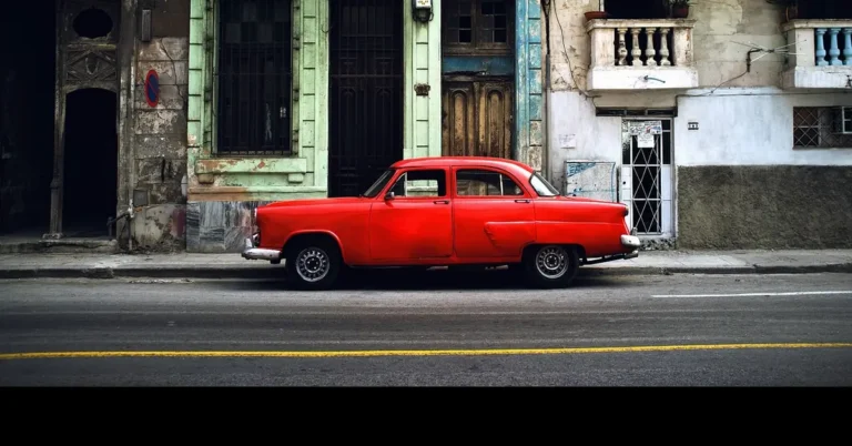 Red vintage car parked in front of weathered buildings on a city street